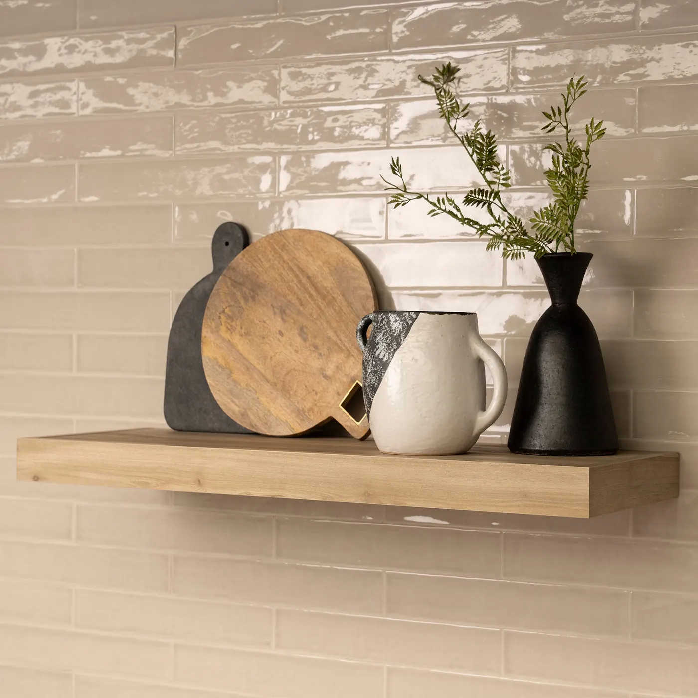 A styled floating shelf on a tiled kitchen wall with boards and ceramics. Photo from murphydoor.com.