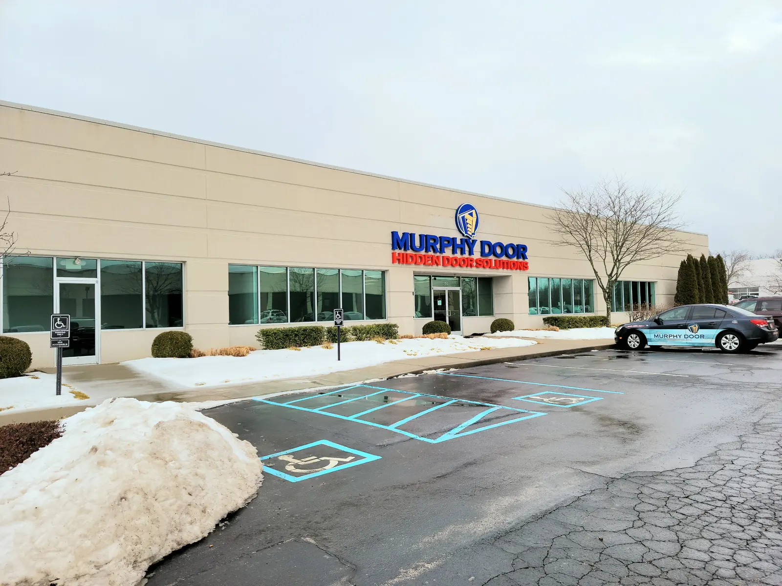 A Murphy Door® manufacturing facility exterior in winter, with a branded company car out front. Company photo.