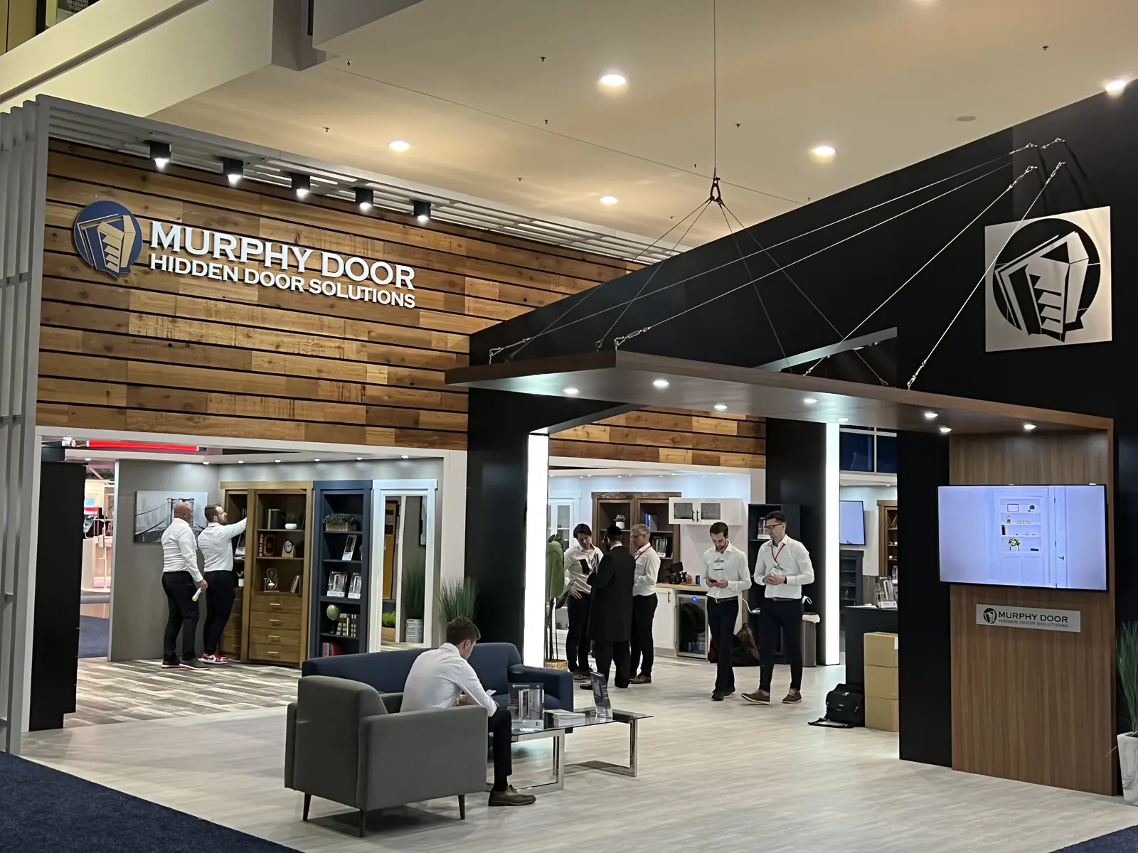 The Murphy Door® booth at the International Builders&rsquo; Show, wood-clad entry with hidden door displays and visitors. Company photo.