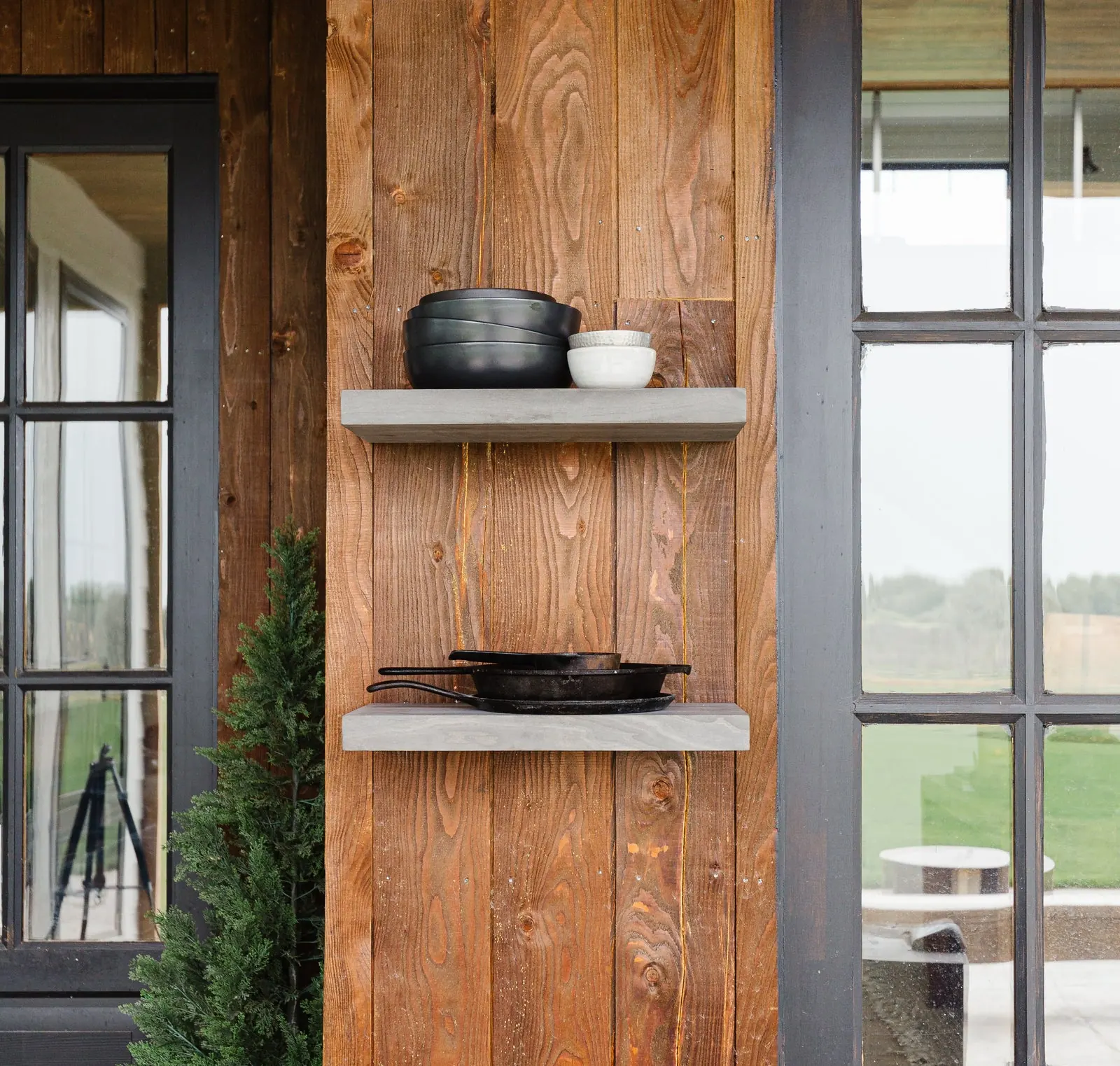 Textured wood-paneled wall with floating shelves and styled ceramics beside black steel windows. Photo from ultrashelf.com.